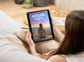 Person holding a tablet with a book cover displayed on a living room couch.